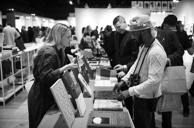 Vendor and customer interaction at a crowded indoor market or convention with multiple booths.