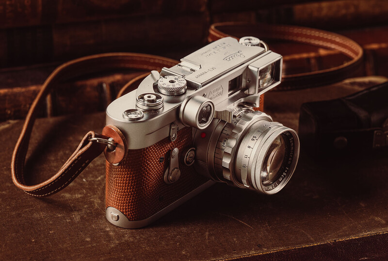 Vintage rangefinder camera with brown leather grip and attached leather strap on warm-toned surface.