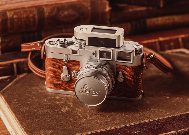 Vintage Leica rangefinder camera with brown leather case and flash attachment on antique books.