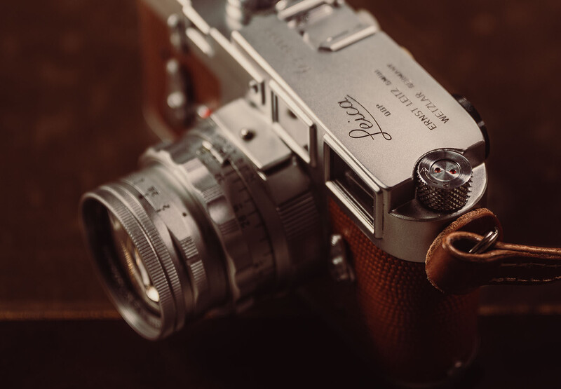 Vintage rangefinder camera with attached lens and brown leather strap against dark background.