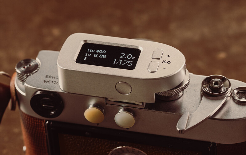 Rangefinder camera with white top plate displaying exposure settings on small digital screen.