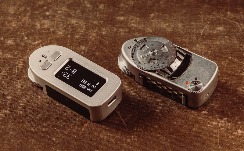A digital light meter and vintage mechanical light meter displayed side by side on a textured brown surface.