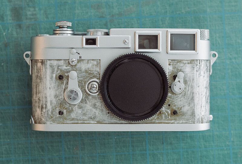 Vintage rangefinder camera with weathered silver body and large black lens against turquoise background.