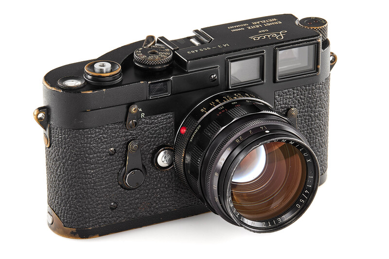 Leica M6 rangefinder camera with black body, textured grip, and fast 50mm lens against white background.