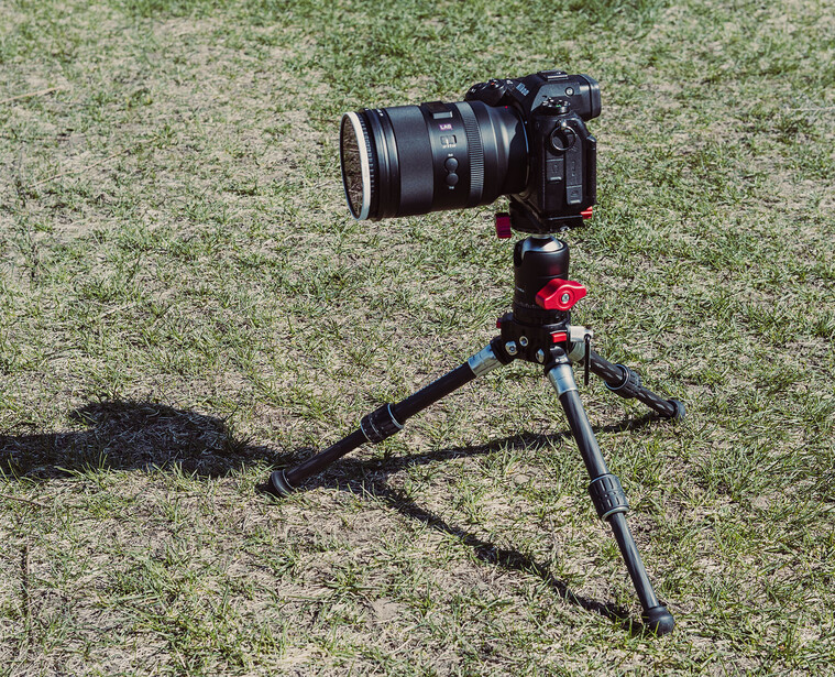 DSLR camera with telephoto lens mounted on a red tripod head, positioned on grass.