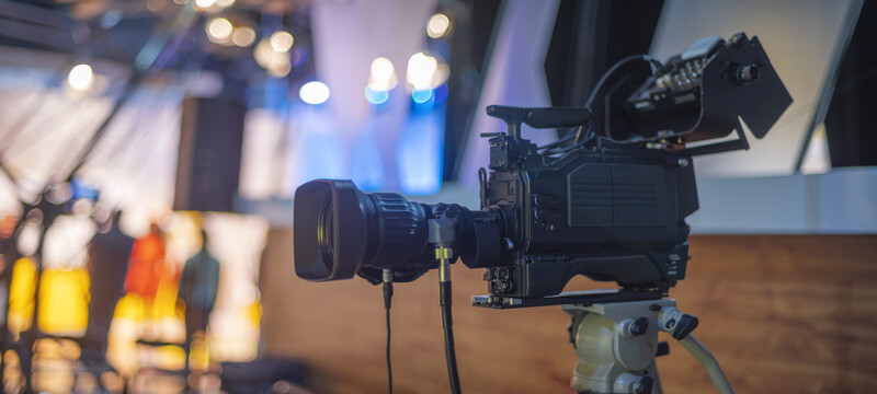 Professional cinema camera mounted on tripod with warm and cool studio lighting in blurred background.