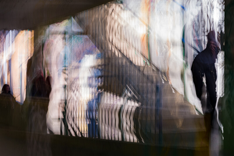 Silhouetted figure standing before layered, motion-blurred projection of faces and vertical lines.