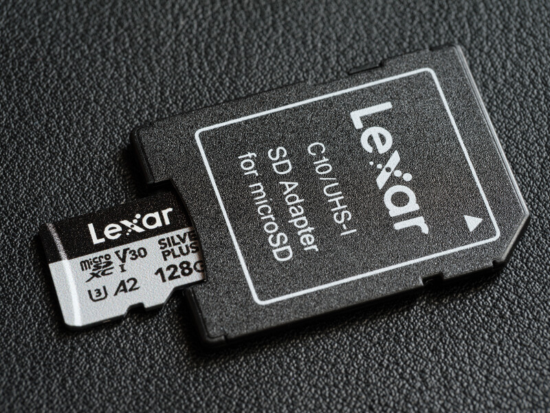 Lexar 128GB microSD card with SD card adapter on textured dark surface.