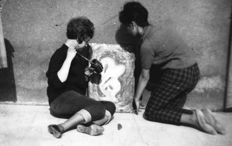 Two people kneeling on the ground examining a sketch or drawing together.