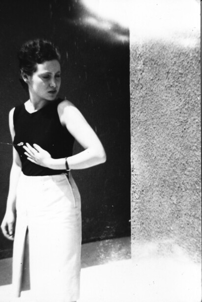 Woman in sleeveless dark top and light-colored skirt standing against contrasting black and white backdrop.