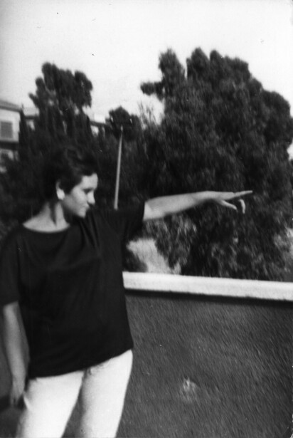 Woman in dark clothing pointing at framed landscape painting on wall.