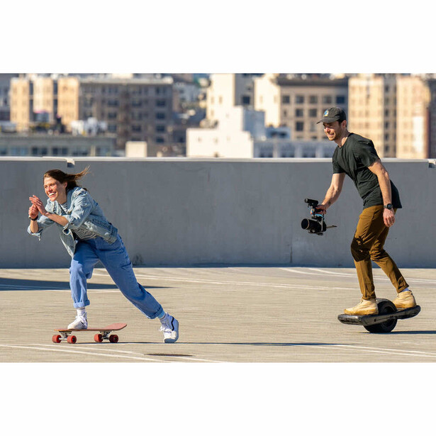 Skateboarder in denim performing trick while photographer in dark clothing captures the shot on urban rooftop.