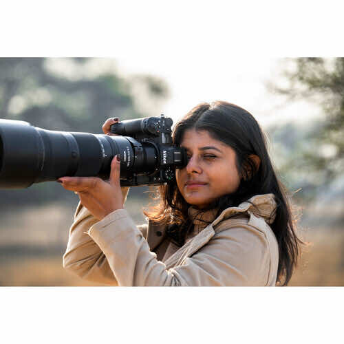 Female photographer holding a DSLR camera with a large telephoto lens, looking through the viewfinder.