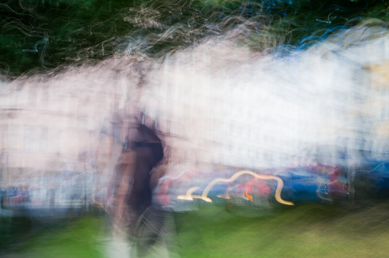 Person in motion blur standing before illuminated carnival rides at dusk.