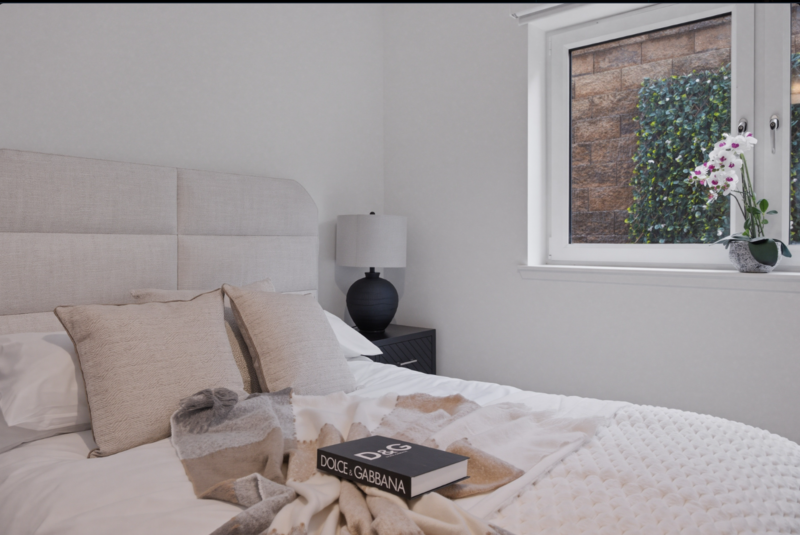 Minimalist bedroom with white padded headboard, cream bedding, and styled nightstand with black lamp and books.