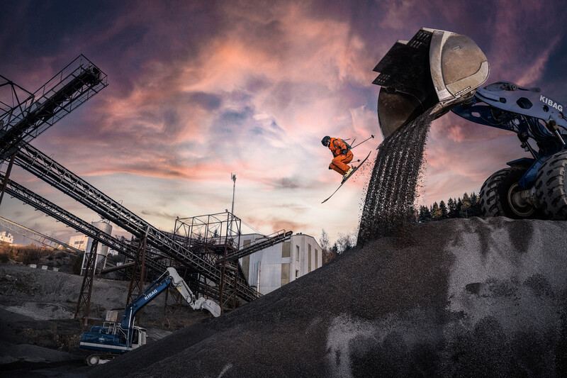 Worker operating heavy machinery to dump aggregate into an industrial pit during golden hour.