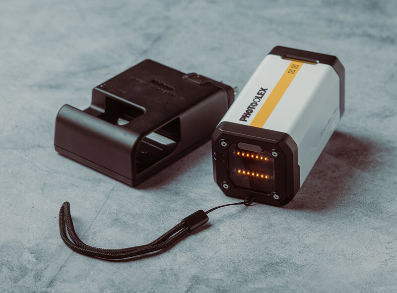 External camera flash with battery pack and charging dock on neutral surface.