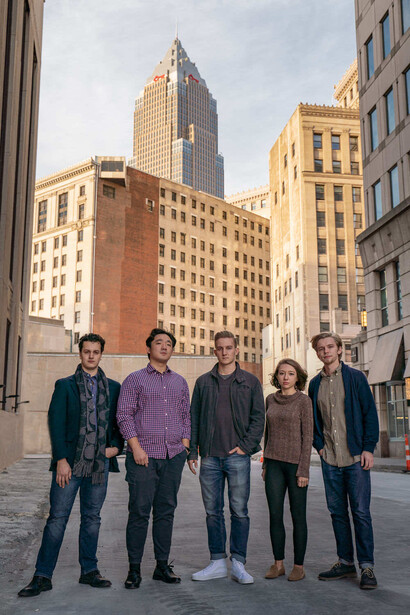 Five people standing in an urban plaza with tall buildings behind them during golden hour.