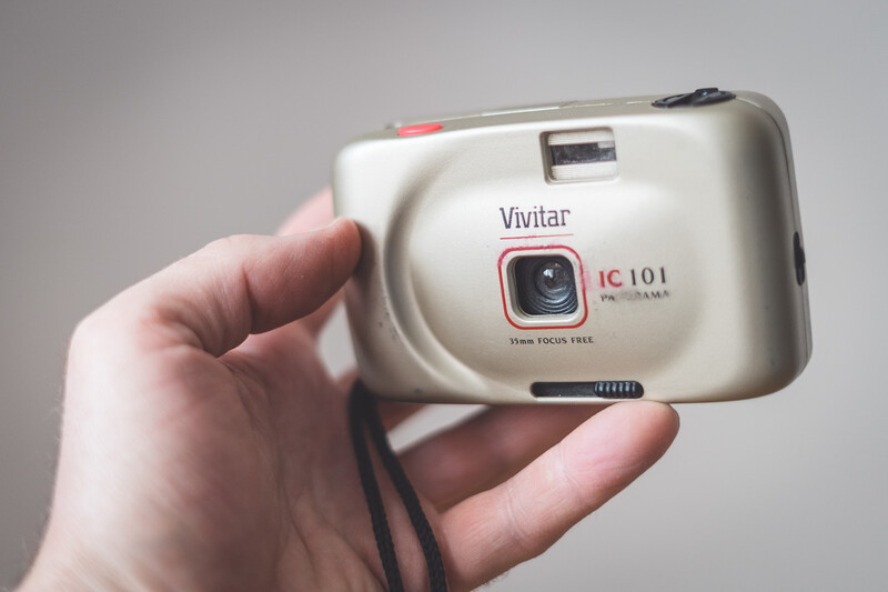 Vivitar IC 101 point-and-shoot film camera held in someone's hand against a neutral gray background.