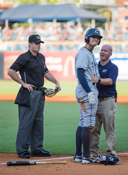 Baseball umpire in black uniform conferring with player and official at home plate