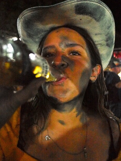 Portrait of woman wearing cowboy hat with face paint and party confetti, lit by warm artificial light