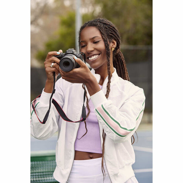 Smiling woman holding vintage rangefinder camera, wearing white jacket outdoors