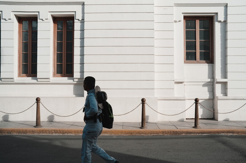 Person in blue jacket walking past white building with rope barrier