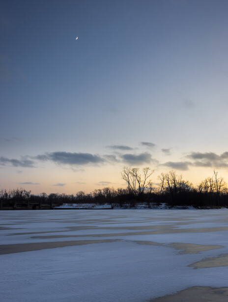Photo of moon hanging over frozen lake at sunset