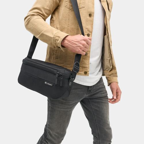 Man wearing tan jacket and black shoulder bag over white t-shirt and gray jeans