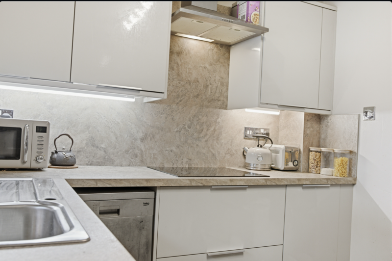 Modern kitchen interior with white cabinetry, marble backsplash, and stainless steel appliances