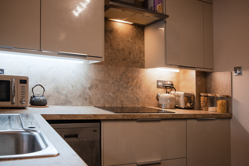 Modern kitchen interior with warm accent lighting illuminating textured backsplash and open shelving