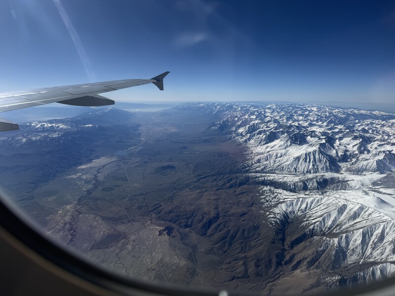 Aerial view from aircraft window showing snow-capped mountain range and wing