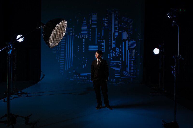 Man in business suit standing on blue-lit stage with cityscape backdrop and studio lighting