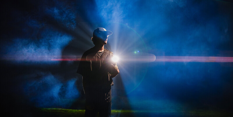 Person in cap and dark jacket backlit by dramatic blue and red light streaks in atmospheric smoke
