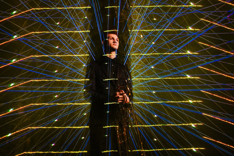 Person silhouetted against symmetrical light trails radiating outward in yellow, blue, and orange