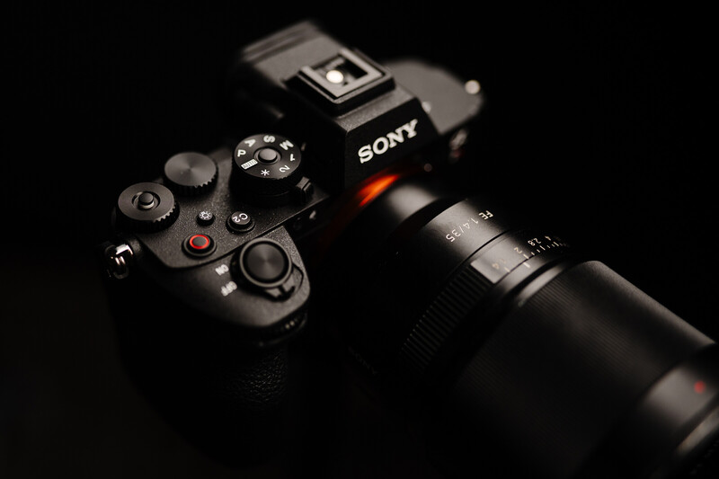 Sony mirrorless camera with attached telephoto lens and wireless remote controller on black background