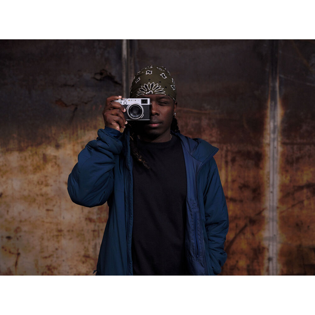 Photographer holding vintage rangefinder camera with ornate headpiece against weathered industrial backdrop
