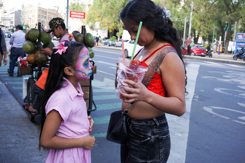 Woman applying colorful face paint to young girl's face on urban street