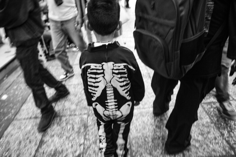Child wearing skeleton costume walking through crowd in black and white