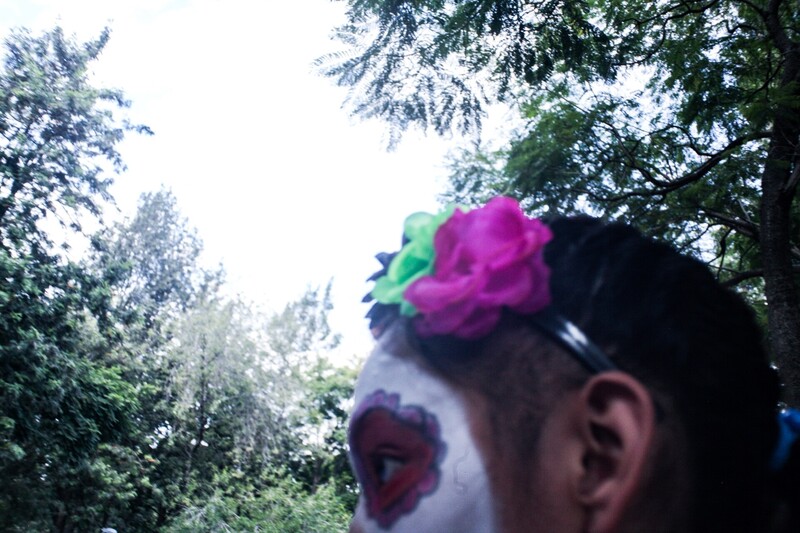 Person with face paint and colorful flower headpiece in forest setting