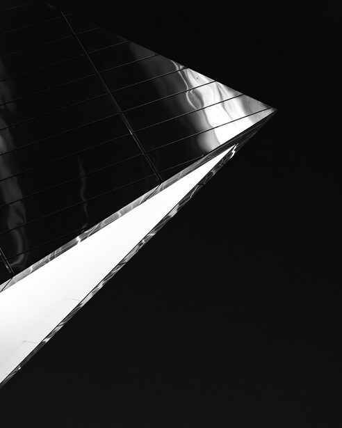 High-contrast black and white architectural photograph of a modern building's angular facade shot from below