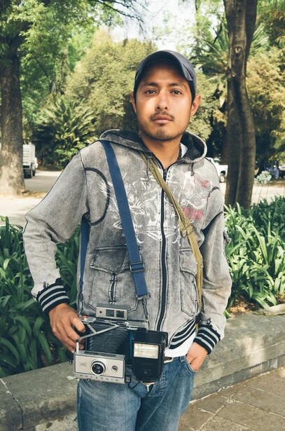 Male subject wearing denim vest and hooded jacket in outdoor park setting