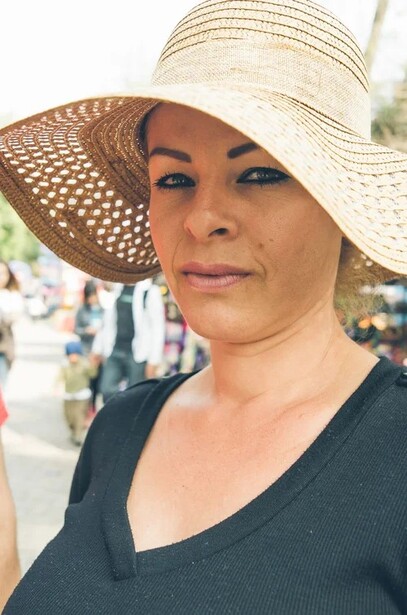 Woman wearing a cream and tan wide-brimmed sun hat with a black v-neck shirt