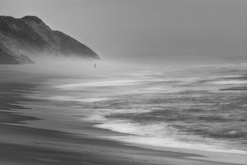 Misty coastal beach with dramatic cliffside and long exposure wave motion