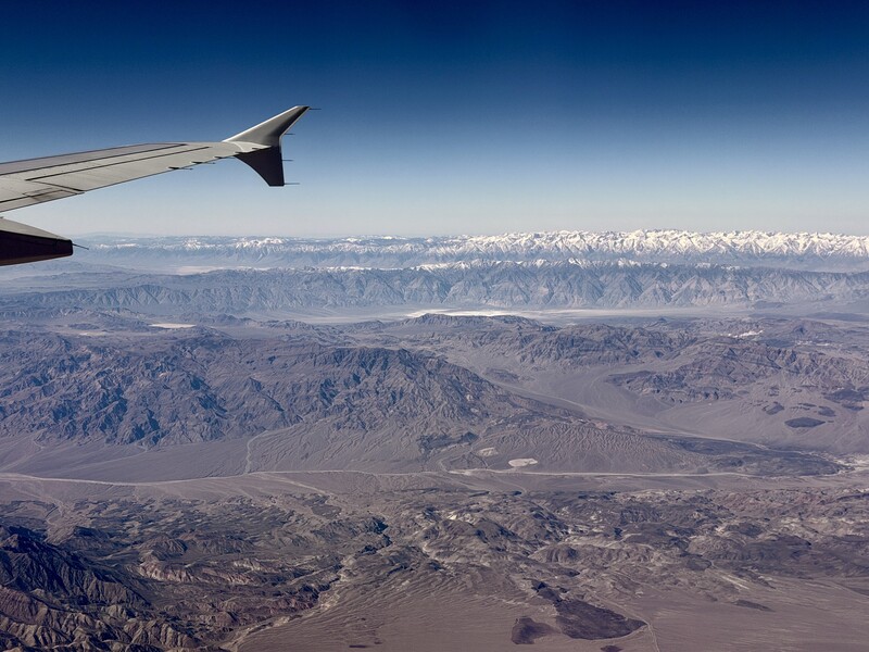 Aerial view from aircraft window showing snow-capped mountain range with valley plains below