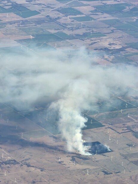 Aerial view of industrial facility with smoke plume rising into clear sky above patchwork farmland