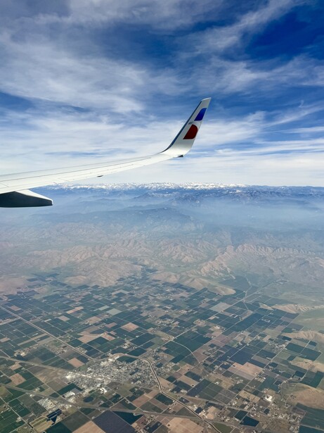 Aircraft wing and fuselage banking over patchwork agricultural landscape and distant mountains