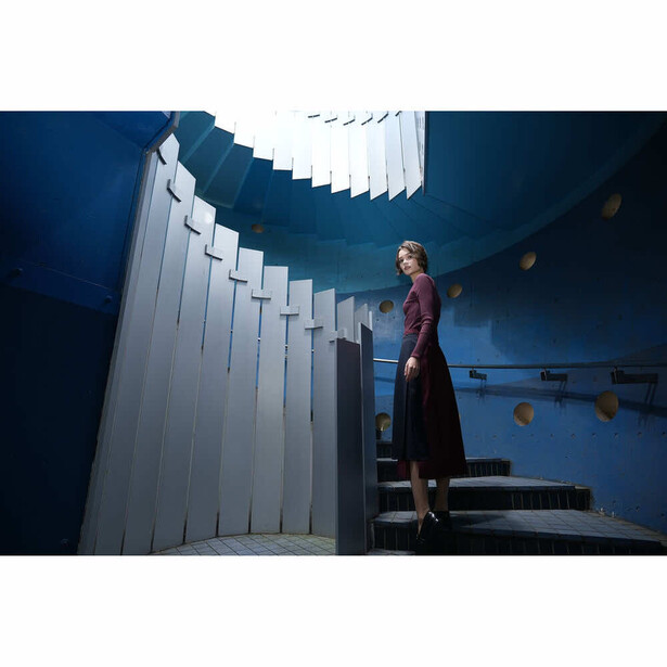 Woman in burgundy dress standing on modern staircase with dramatic blue lighting