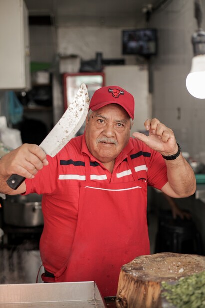 Man in red uniform and cap holding up a decorative white paper banner indoors
