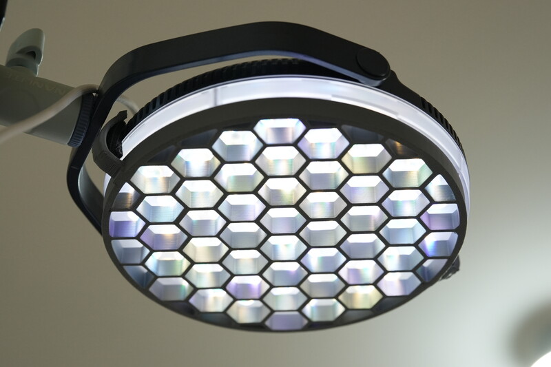 Ceiling-mounted LED surgical light with hexagonal panel array and adjustable arm